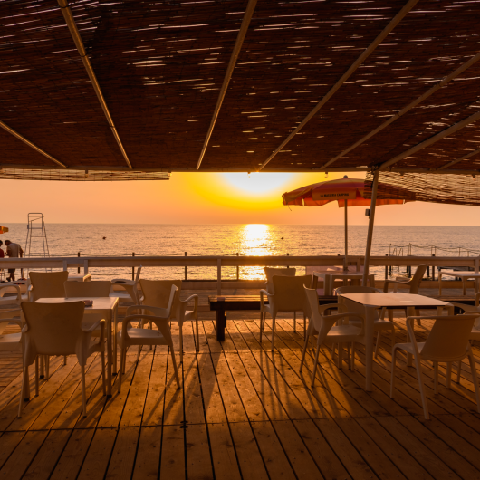 Sunset on a terrace with sea view, chairs and umbrellas.