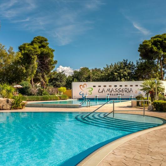 Piscina all'aperto a La Masseria Gallipoli, circondata da palme e giardini.