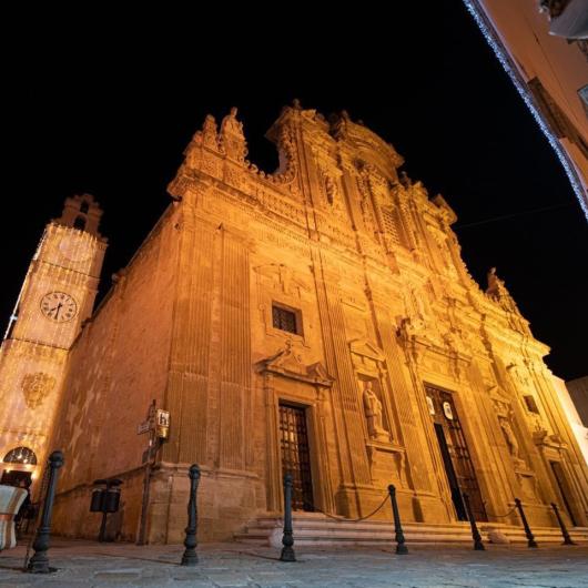 Chiesa barocca illuminata di notte, con torre dell'orologio decorata.