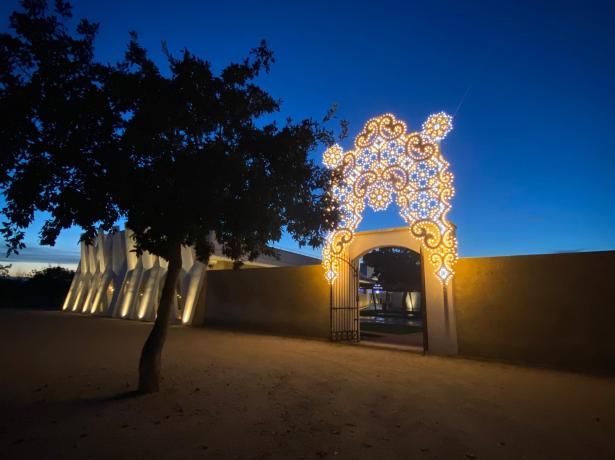 Portale illuminato al tramonto con decorazioni luminose e albero in primo piano.