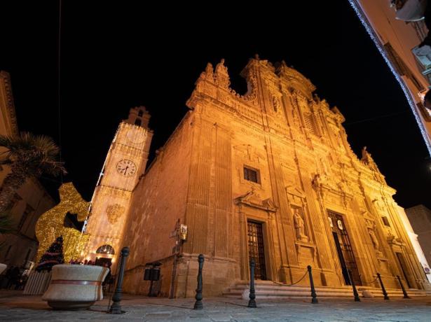 Chiesa barocca illuminata di notte, con torre dell'orologio decorata.