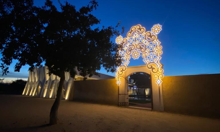 Portale illuminato al tramonto con decorazioni luminose e albero in primo piano.