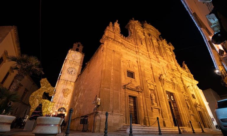 Chiesa barocca illuminata di notte, con torre dell'orologio decorata.